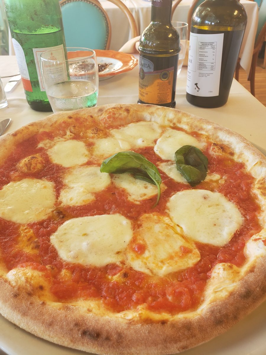 A Margherita pizza on a white tablecloth, olive oil bottle beside it