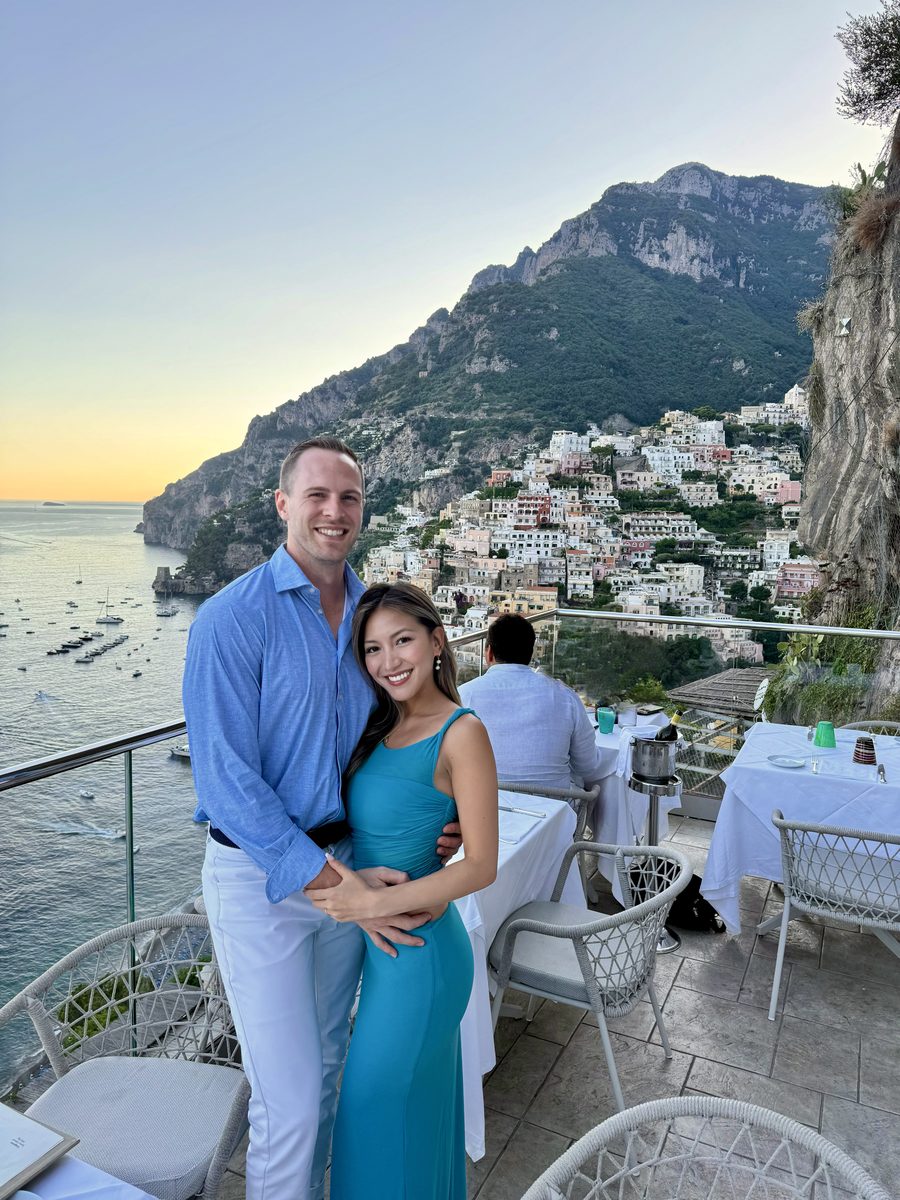 Linda and Collin on a cliffside terrace at sunset, coastal village behind