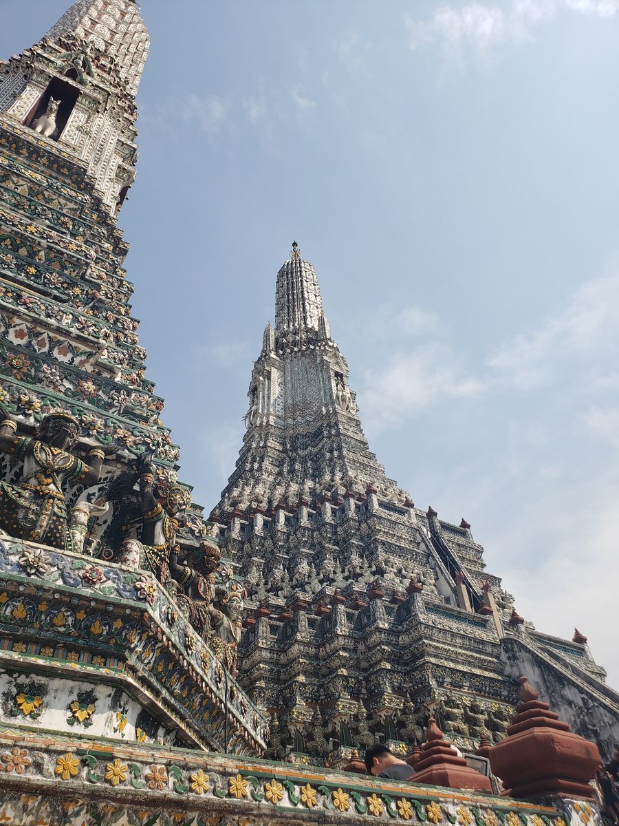 Two porcelain-covered prangs of Wat Arun against a pale blue sky